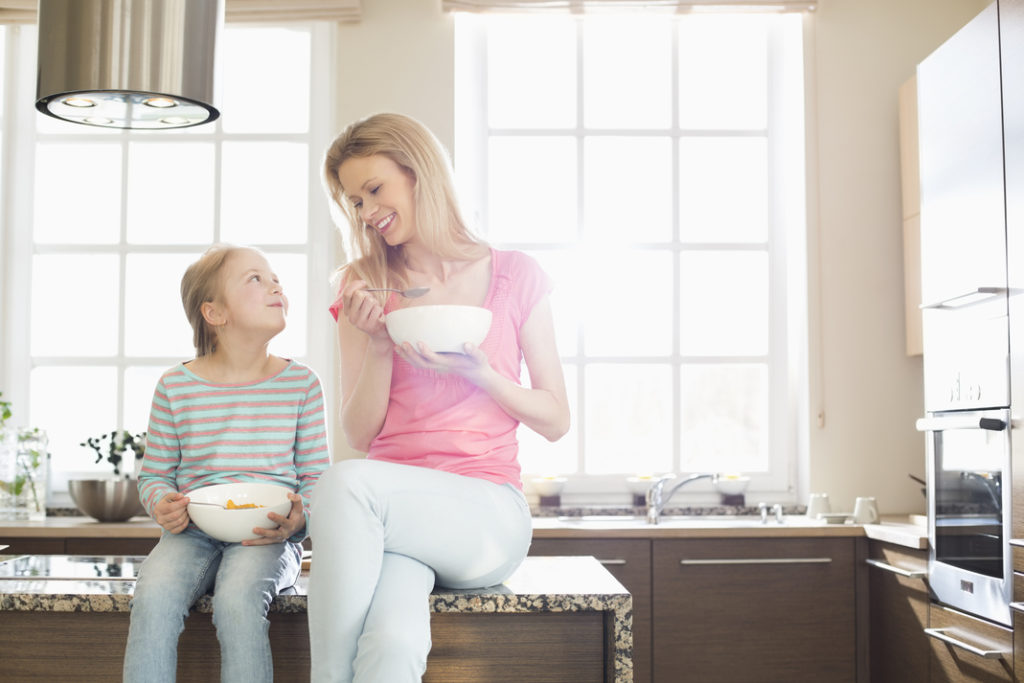 Happy mother and daughter having breakfast in kitchen