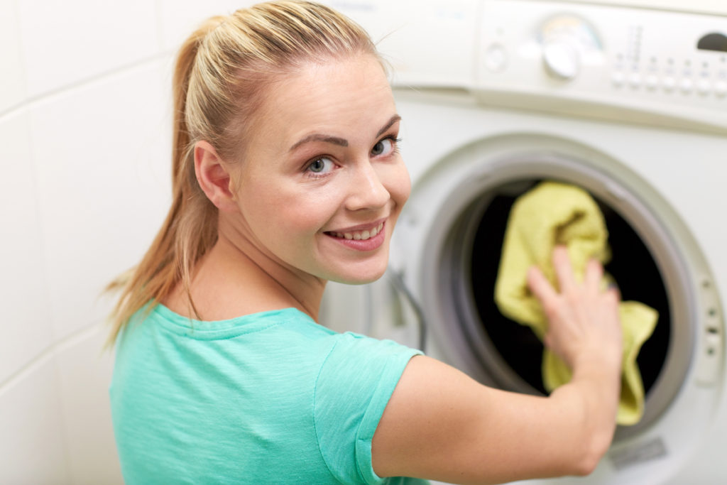 happy woman putting laundry into washer at home