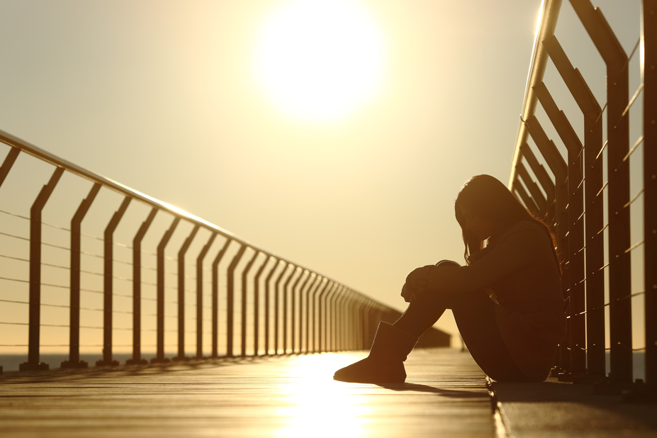 Sad teenager girl depressed sitting in the floor of a bridge on the beach at sunset